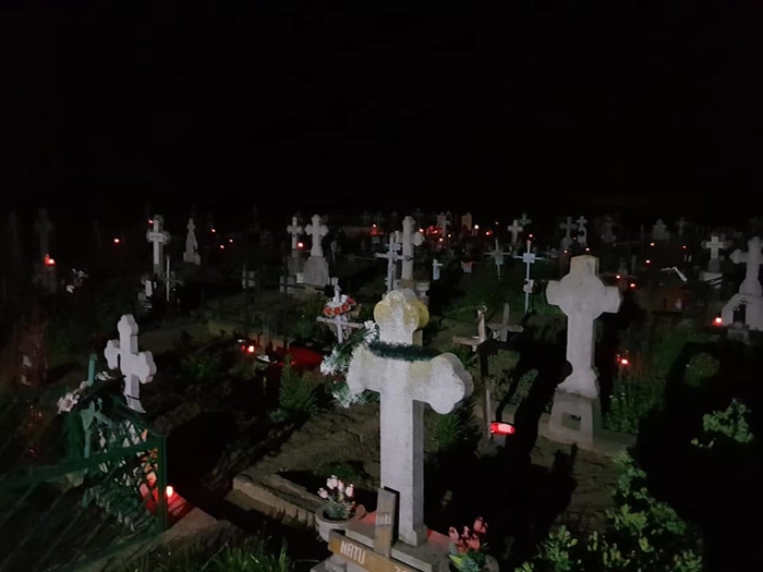 cruci cu luminari care ard intr-un cimitir, pe timp de noapte