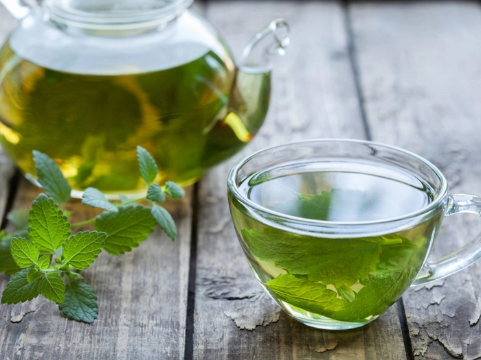 o cana de ceai cu menta langa un ceainic cu ceai si o frunza de menta
