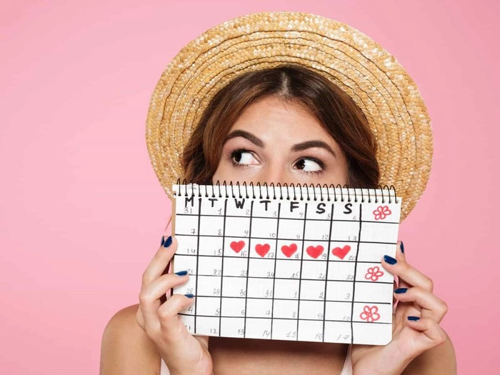 femeie care tine in mana un calendar in care are insemnat perioada ciclului menstrual