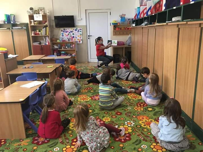 copii aflati in sala de clasa si educator care le arata o carte