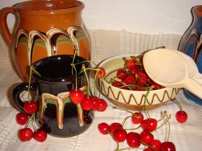 o imagine cu mai multe vase de lut si cateva cirese