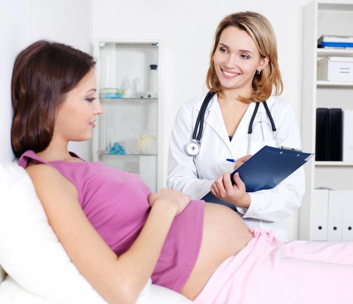 medic care discuta cu o femeie insarcinata care sta culcata pe un pat de spital
