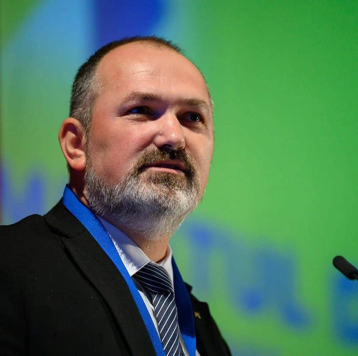 Marius Danga in costum negru si cravata albastra in fata unui microfon