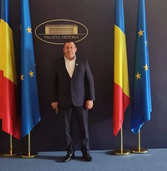 Mihai Balan in costum negru si steagul UE si al Romaniei