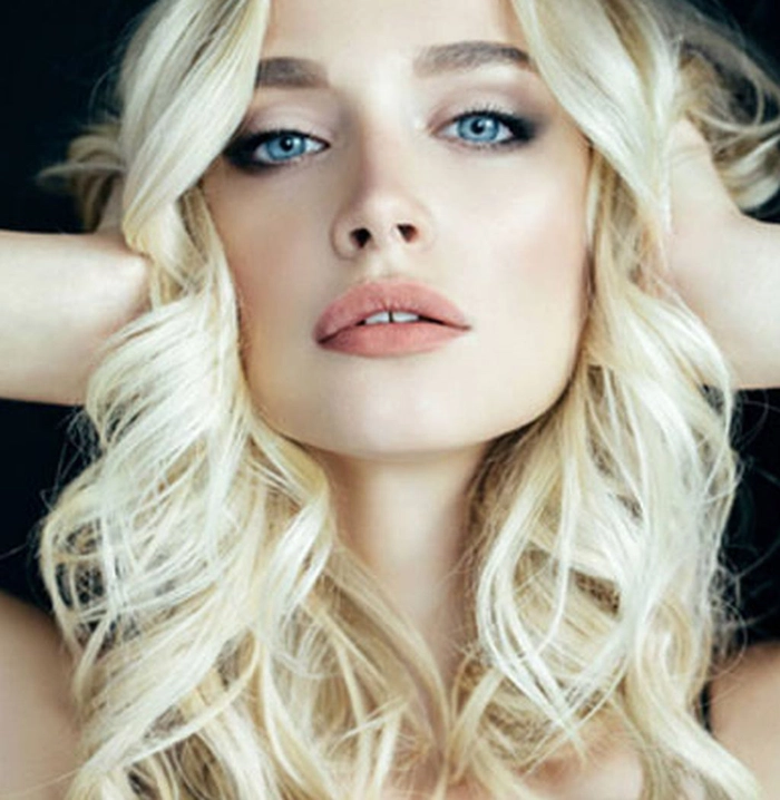 femeie cu paru blond care zambeste si isi tine mainele in cap