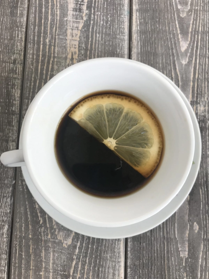 o ceasca de cafea langa o bucata de lamaie pe o masa