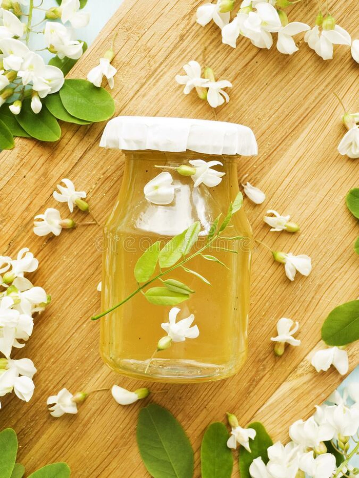un borcan cu sirop de salcam pentru iarna inconjurat de mai multe flori de salcam