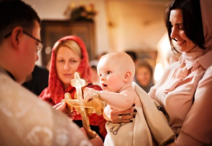 bebelus care este tinut in brate de nasi in fata unui preot in biserica