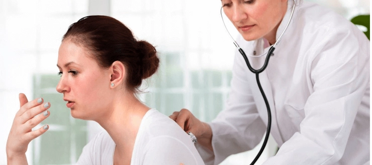 medic care asculta cu un stetoscop plamanii unei femei care tuseste