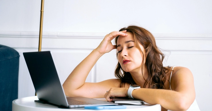 femeie care sta in fata unui calculator si se tine de cap din cauza durerii