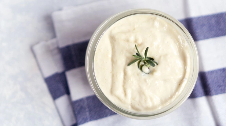 un bol cu sos aioli decorat cu verdeata pe o masa