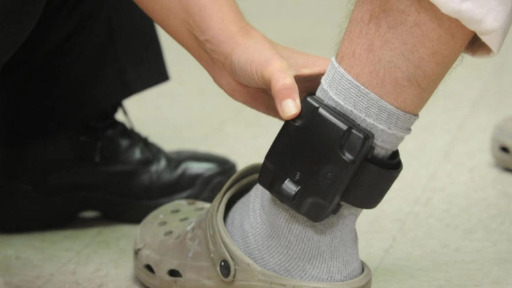 Piciorul unui barbat la care este atasat un sistem specific arestului la domiciliu, verificat de catre o alta persoana