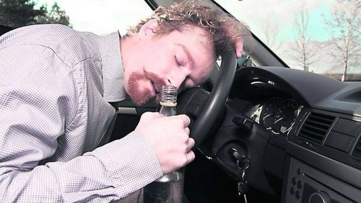  barbat doarme cu capul pe volanul masinii, are in mana o sticla de alcool