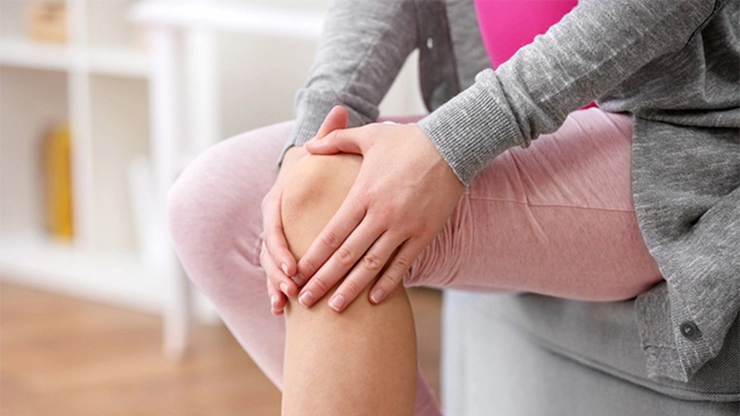 femeie care se tine de genunchi din cauza poliartritei reumatoide