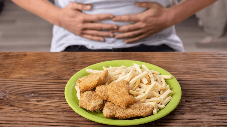 persoana care se tine de burta si in fata sa pe o masa are o farfurie cu fast food