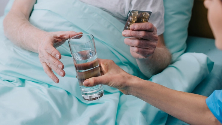 medic care intinde un pahar cu apa unui pacient care tine in mana pastile
