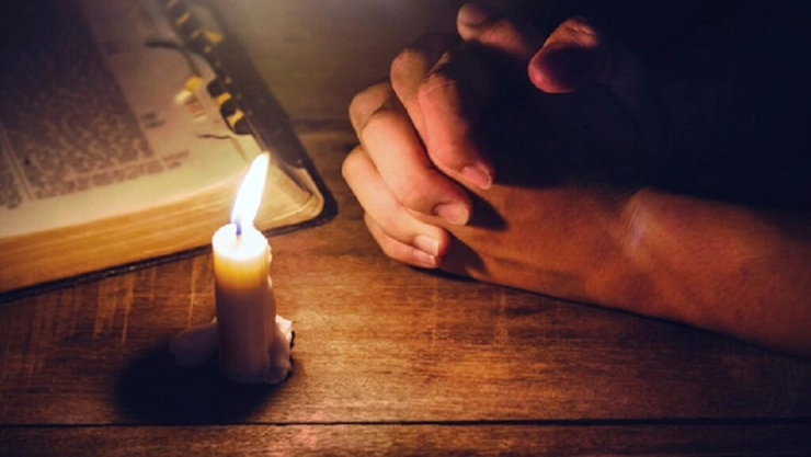 persoană care roagă cu lumânarea aprinsă