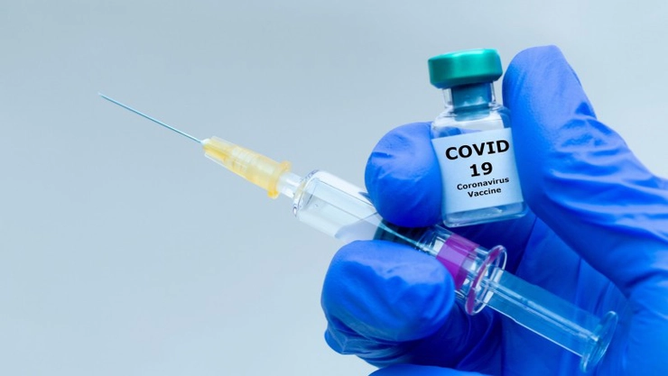  o mana cu manusa albastra care tine o seringa si o doza de vaccin anti-Covid-19