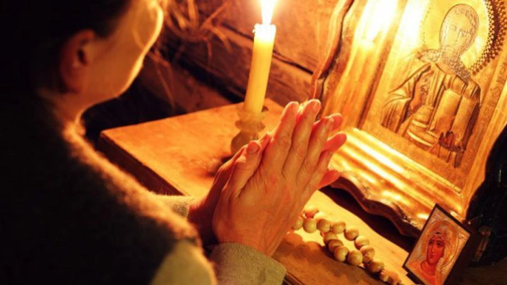 o femeie care se roagă în fața unei icoane și a unei lumânări aprinse