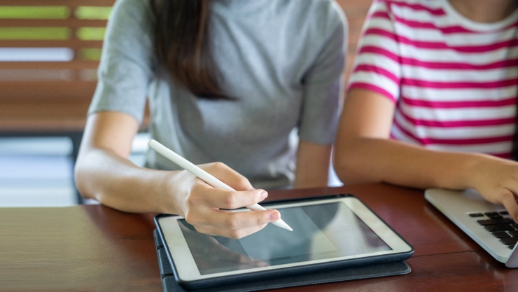 doua persoane in tricou asezate la un birou cu tableta si laptop in fata