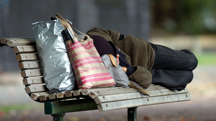 o imagine cu un om al strazi care doarme pe o banca