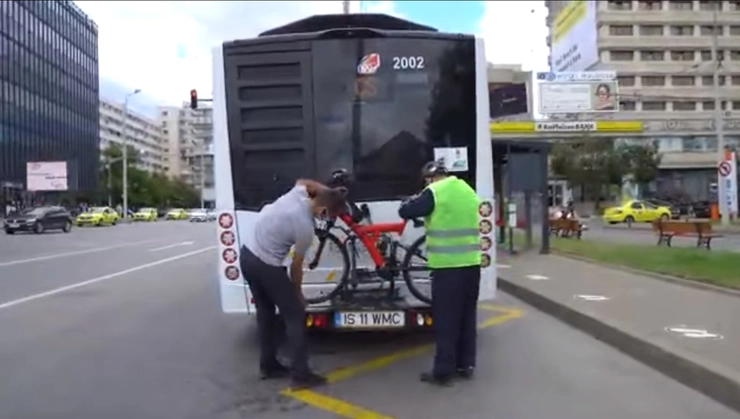  doua persoane in spatele unui autobuz sustin o bicicleta