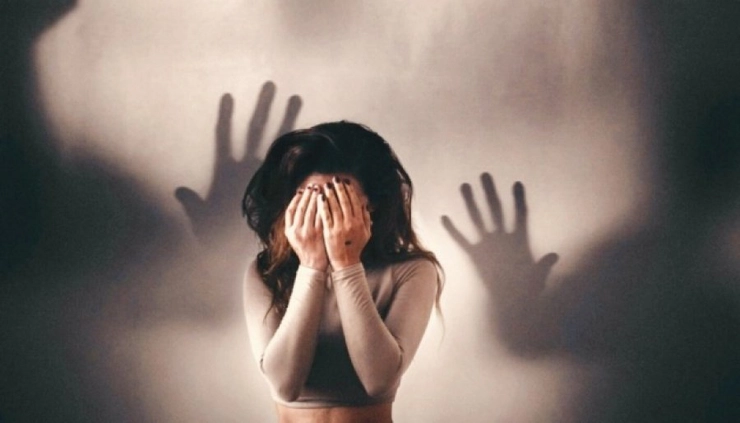 femeie care isi acopera fata cu mainele si pe peretele din spate apar doua maini