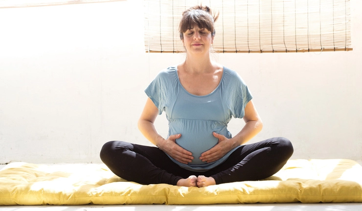 femeie insarcinata care face yoga si se tine de burta