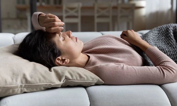 femeie care sta culcata pe pat si tine mana pe cap din cauza durerilor
