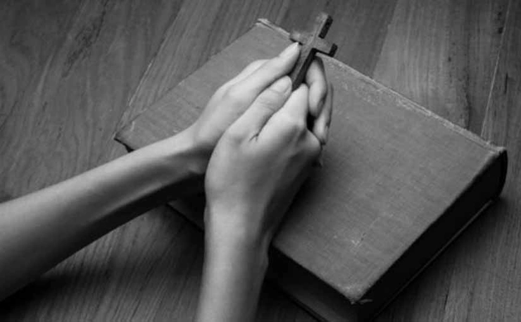 mâini care țin o cruce și se sprijină pe o carte