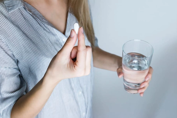 o femeie care ia o aspirină cu un pahar cu apă