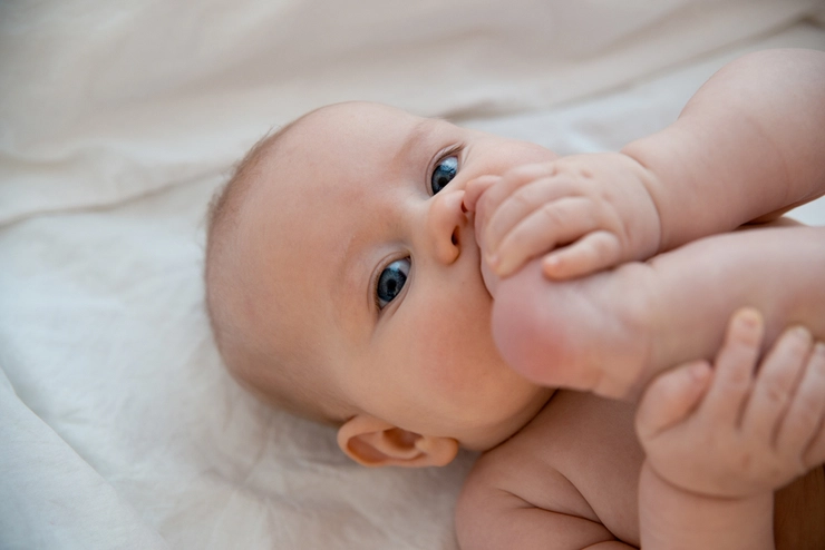 bebeluș care își ține piciorul la gură