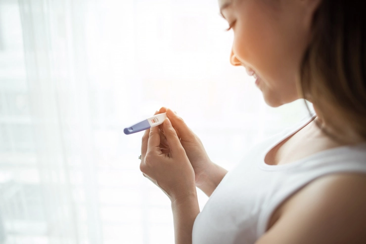 femeie care priveste un test de sarcina si zambeste