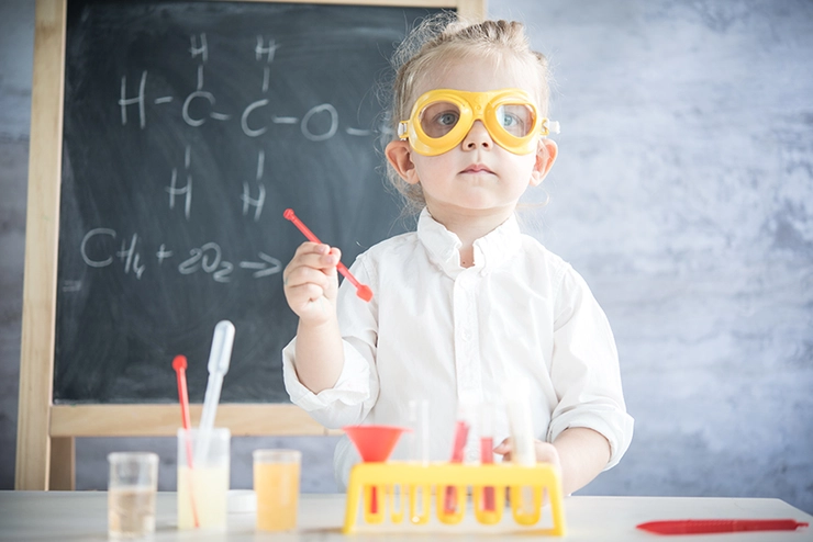copil care are ochelari si echipament din jucarie de chimist fiind intr-o sala de clasa