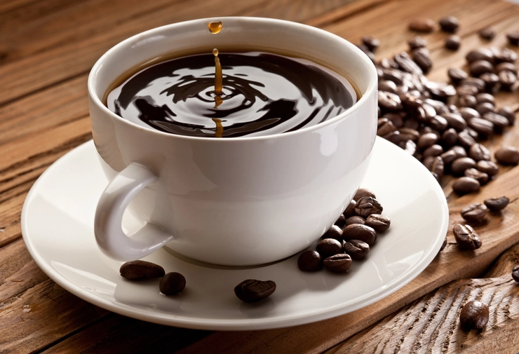 ceasca de cafea pe farfurie langa boabe de cafea