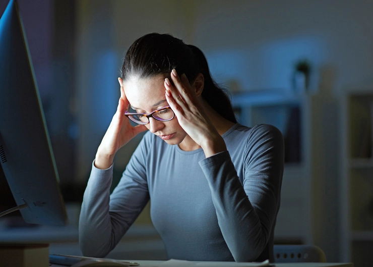 femeie care sta in fata unui calculator si se tine de cap din cauza anxietatii